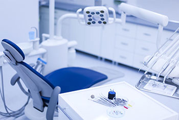 The image displays a modern dental clinic with a blue chair, dental equipment, and a clean, sterile environment.