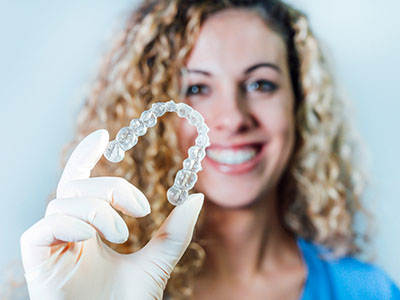 A woman is holding a large, transparent dental retainer.