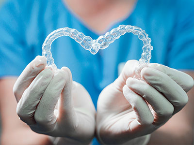 A dental professional s hands holding a transparent heart-shaped dental retainer.