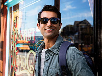A young man wearing sunglasses and a backpack, standing in front of a store window.
