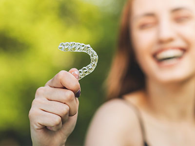 A smiling woman holding a clear plastic dental retainer in her hand.