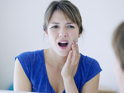 A woman with a distressed facial expression, possibly indicating pain or discomfort, is looking at her reflection in a mirror.