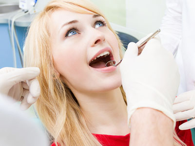 Woman sitting in dental chair with open mouth, receiving dental care.