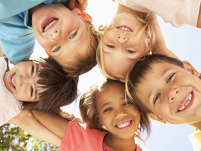 A group of children, likely a family, smiling and posing together in a casual outdoor setting.