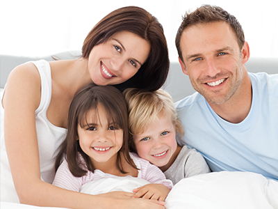 A family of five, including a man and woman with three children, poses for a photo in a bedroom setting.