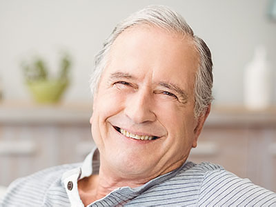 The image shows an elderly man with a smile, sitting comfortably in a chair.