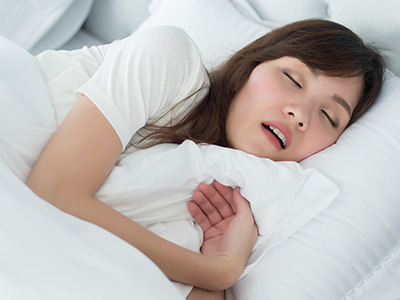 A young woman is lying in bed with her eyes closed, appearing to be asleep or resting.