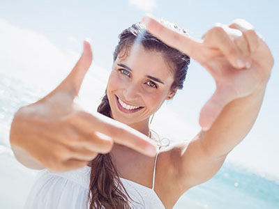 Woman with long hair, smiling at camera, holding up index finger in front of face.